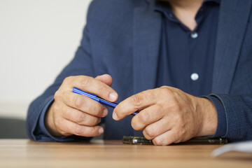 Elegant adult man holding a fountain pen in his hand while sitting at a table next to a smartphone...