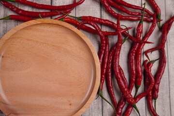 empty wooden plate on corner surrounded by red chili peppers