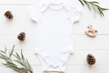Baby bodysuit Christmas or winter mockup. Blank white baby bodysuit on a wood background with plants and cones, flat lay, copy space.