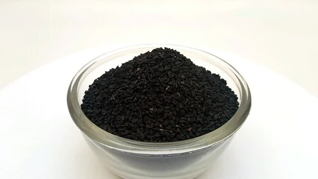 Black cumin seeds or black caraway seeds in a glass bowl isolated rotating on white background, a glass bowl full of Black cumin seeds or black caraway seeds in the center frame, zooming in