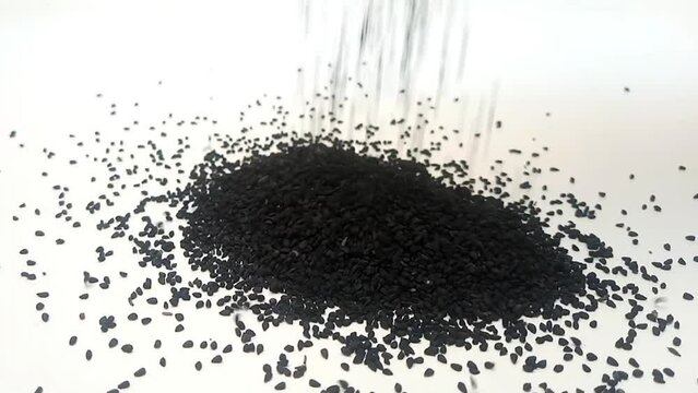 Black cumin seeds or black caraway seeds falling on clean white background in the center frame, close up, herbs and spices