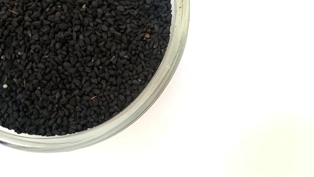 Black cumin seeds or black caraway seeds in a glass bowl isolated rotating top left corner, a glass bowl full of Black cumin seeds or black caraway seeds on white background, close up