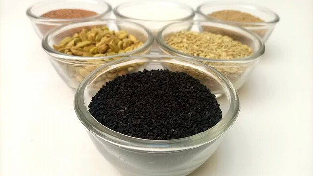 Focusing in a bowl of Black cumin seeds or black caraway seeds with assortment of aromatic spices and herbs in glass bowls in the background, close up, front view
