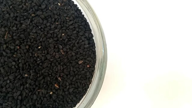 Half of circle shaped Black cumin seeds or black caraway seeds glass bowl in the left half of the frame, rotating, isolated on the white background, closeup, herbs and spices