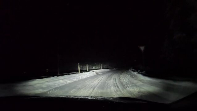 Driving on snowy road at night in forest.