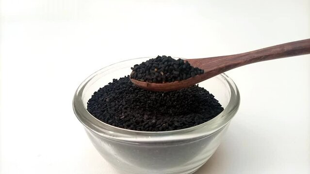 Spoon out of Black cumin seeds or black caraway seeds from the glass bowl with a wooden spoon, herbs and spices