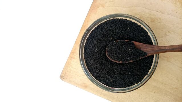 Taking Black cumin seeds or black caraway seeds from the glass bowl with a wooden spoon, top view, herbs and spices