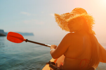 A woman wearing a straw hat is paddling a canoe on a sunny day. Scene is relaxed and carefree, as...