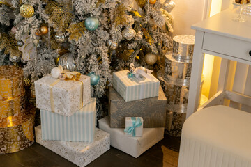 A Christmas tree with many gifts stacked on top of it. The gifts are wrapped in white paper and blue and gold ribbons.