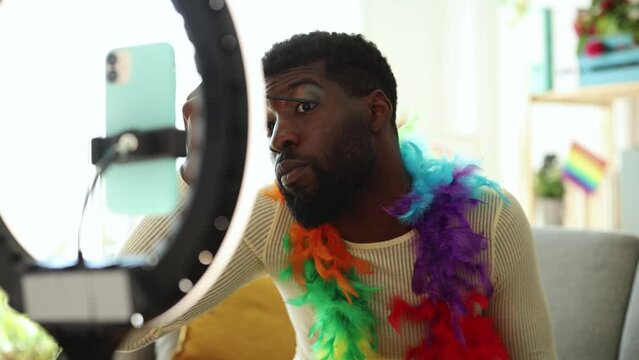 Man Experimenting with Bold Makeup Colors During a Self-Styling Session - An African American man applies vibrant eye makeup, exploring personal style and self-expression in front of a camera setup.