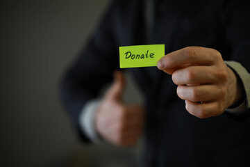 Businessman shows a paper with the word donate. Charitable donation in business concept.