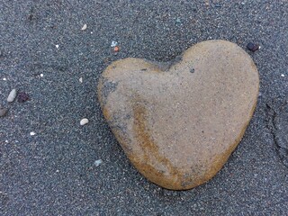 Big sea pebble stone or rock in heart shape as frame on beach. Pebble stone heart natural abstract texture or background frame. Pebble stone heart frame on seacoast. Brown pebble heart in sand frame