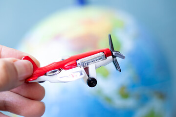 Flight idea concept. Man hand holding toy propeller plane in front of earth background.