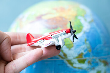 Hand holding toy propeller plane on earth background. Aviation idea concept. Air transportation. 