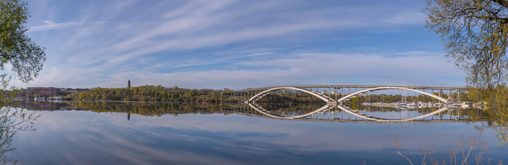 Fototapeta premium Panorama view at the calm bay Riddarfjärden, the long bridge Västerbron in the district Kungsholmen, a sunny summer morning in Stockholm