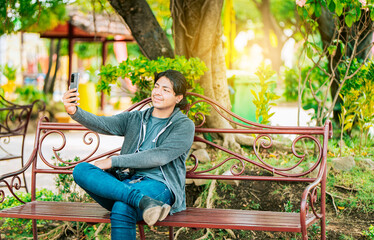 Smiling man sitting on a bench taking a selfie in Nagarote Park. Relaxed guy taking a selfie sitting on a bench in Nagarote Park