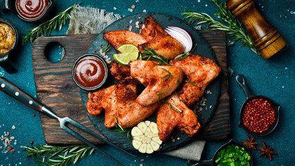Grilled chicken wings with garlic and rosemary on a slate plate. On a dark background.