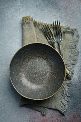 An aesthetic arrangement of vintage dark bowls, plates and cutlery on a gray concrete background....