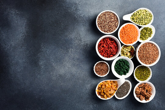 Set of superfoods, cereals, nuts and dried fruits, spirulina and goji in white ceramic bowls. On a gray concrete background. Top view. Free space for text.