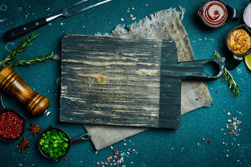 Naklejka premium Kitchen cutting board on table with spices, vegetables and herbs. Free space for a recipe. Rustic style. On a dark background.