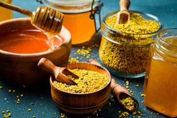 Organic honey in wooden bowl with honey stick and flower pollen. Honey background. Top view.