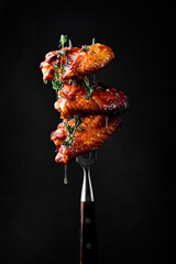 Grilled chicken wings baked in honey sauce on a fork. Honey stick with honey. On a black background.
