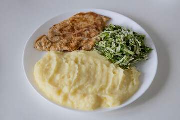 A delicious breakfast or lunch with mashed potatoes, chop with salad - green onions and green young cabbage, parsley on the white plate.
