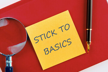 Finance and economics concept. Text STICK TO BASICS on a yellow sticker on a red business notebook in a composition with a magnifying glass and a fountain pen