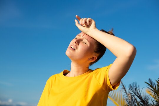 Girl is suffering from heat, woman with heatstroke. Having sunstroke at summer hot weather. Dangerous sun, girl under sunshine. Headache. Person holds hand on head. Feeling bad, unwell, unhealthy