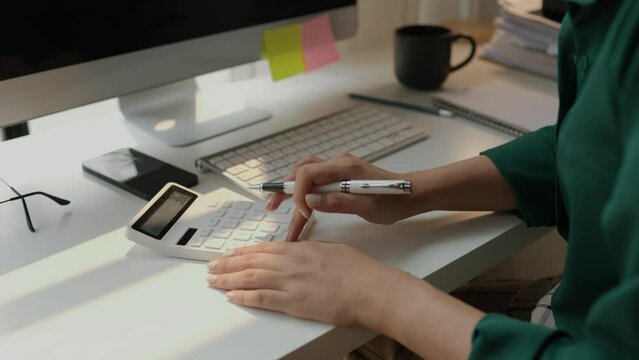 a female accountant is using calculator, head of marketing department is planning to analysis about investment in currency, calculating to pay yearly tax, find the total of the company's expenses