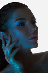 Close-up of a serene woman, her skin sparkling under a soft blue light, gazing into the distance
