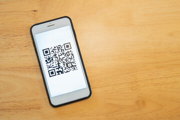 QR Code on mobile screen over wooden background with copy space.