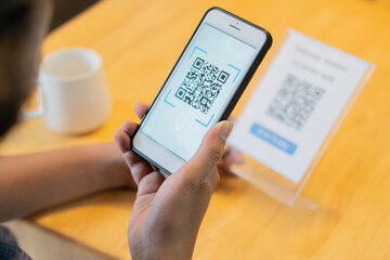 Selective focus of man's hand scanning QR code through mobile phone at cafe table.