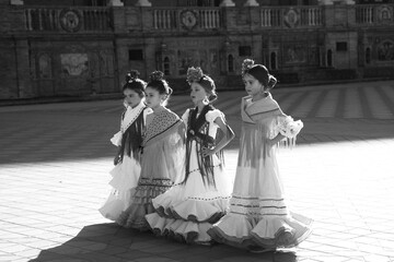 four pretty little girls dancing flamenco dressed in typical gypsy costume pose in a famous square...