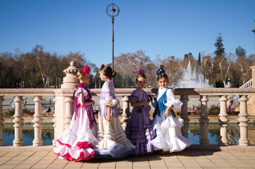 four pretty little girls dancing flamenco dressed in typical gypsy costumes talk to each other in a famous square in seville, spain. Flamenco, cultural heritage of humanity.