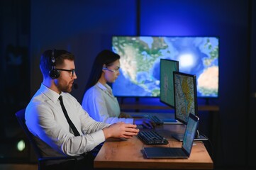 In Monitoring Room Technical Support Specialist Speaks into Headset. His Colleagues are Working in the Background