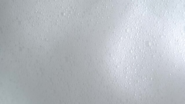 Soap bubbles on window glass. Macro shot of white soap suds flowing down of glass. Shower concept. Cleaning windows, hygiene, disinfection, housework, household, cleanup, washing.