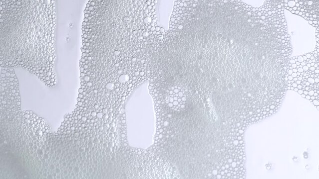 Soap bubbles on window glass. Macro shot of white soap suds flowing down of glass. Shower concept. Cleaning windows, hygiene, disinfection, housework, household, cleanup, washing.
