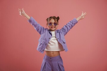 Smiling, with hands up and on the sides. Cute little girl is against pink background