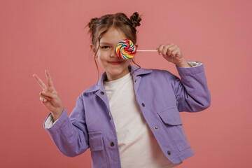 Peace hand gesture, with candy. Cute little girl is against pink background