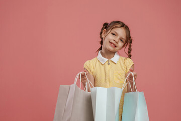 With shopping bags. Cute little girl is against pink background