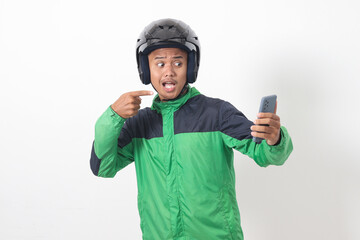 Portrait of Asian online taxi driver wearing green jacket and helmet holding mobile phone while pointing to the side. Isolated image on white background