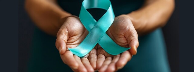 Close-up teal awareness ribbon holded by woman hands to support cancer survivor. Ovarian Cancer month, cervical cancer day.