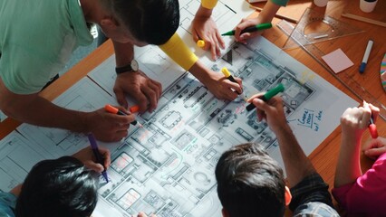 Top view of civil engineer team writing at blueprint at meeting table with color palettes. Group of smart diverse people planning and taking a note while manager looking at project plans. Symposium.