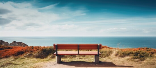 Obraz premium A serene copy space image of a bench with a view of the ocean located near the vibrant Red Cliff on the enchanting island of Sylt