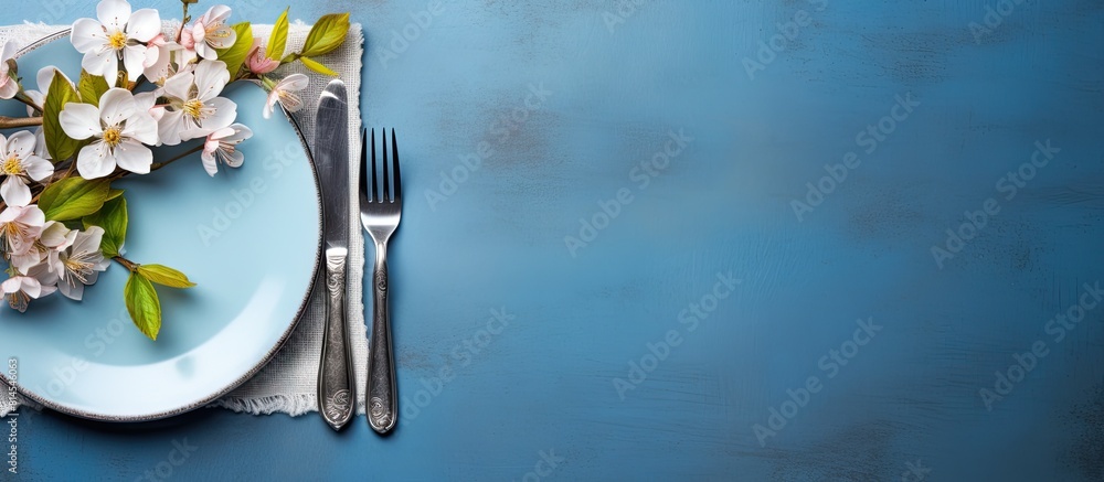 Poster The table is set with silverware a napkin and a flower on a blue background It is a spring themed arrangement seen from above with copy space for an image