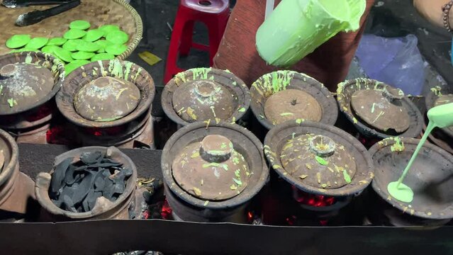 The cake seller pours the green mixture into earthenware containers for cooking