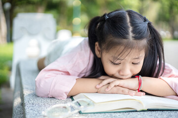 Cute little asian girl reading a book while lying at garden
