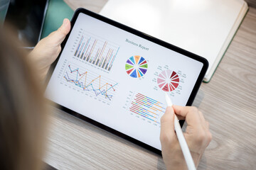 Business woman sitting at table and taking notes in tablet screen graphics and charts