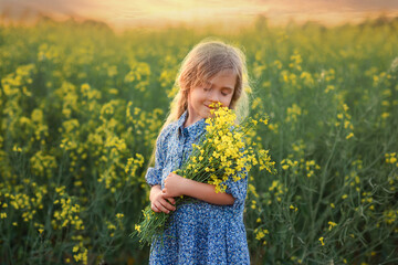 a small beautiful girl in a blue dress with a bouquet of flowers in a rapeseed field is walking for a walk. girl and nature